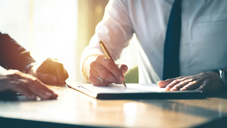 Man signing a document in the presence of others.